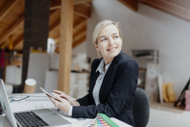 genç kadın mimar laptop ve planları ile çatı katında masada otururken Tablet PC'yi kullanma 