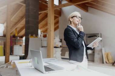 genç kadın mimar dizüstü bilgisayar ve planları loft adlı tablo yakın dururken Tablet PC'yi kullanma 