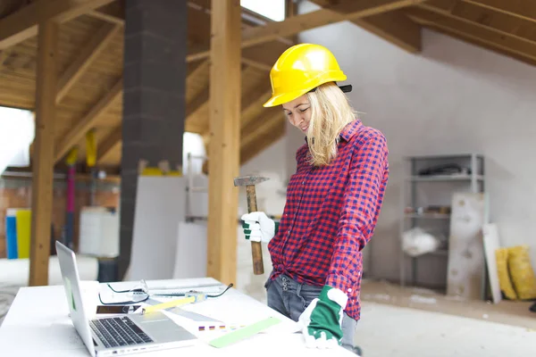 blonde woman with yellow helmet and green gloves planning on laptop expansion of loft