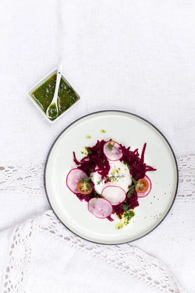 white plate with sheep cheese and beets with radishes on white textile background