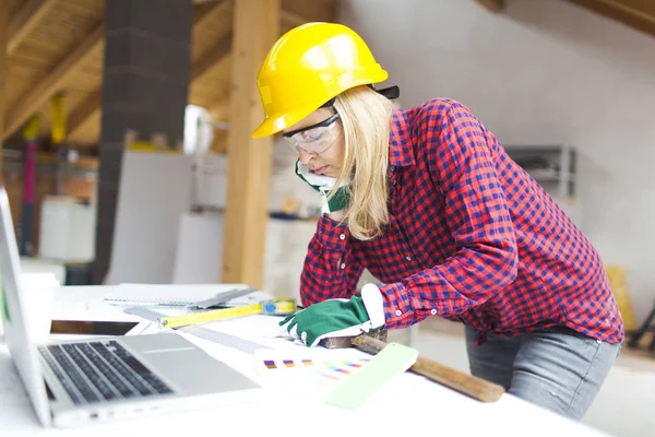 blonde woman with yellow helmet and green gloves planning expansion of loft