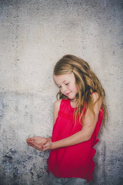 コンクリートの背景の前で両手を開いた赤いブラウス立っている美しい少女 — ストック写真