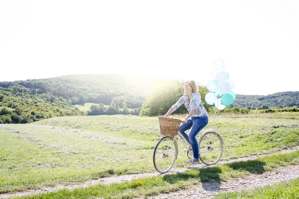 Happy woman riding bicycle with balloons on summer meadow at sunny day