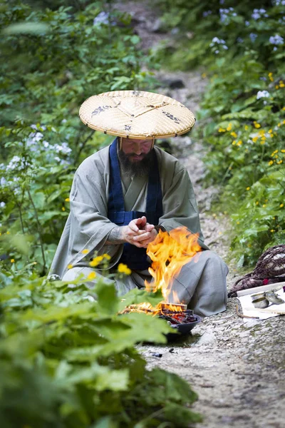 European man with beard and japanese robe making fire ceremony in front of Great Waterfall in Austria