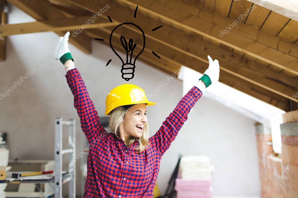 happy blonde female builder in safety helmet standing with raised arms and light bulb icon over head in loft, concept of idea to expand loft 