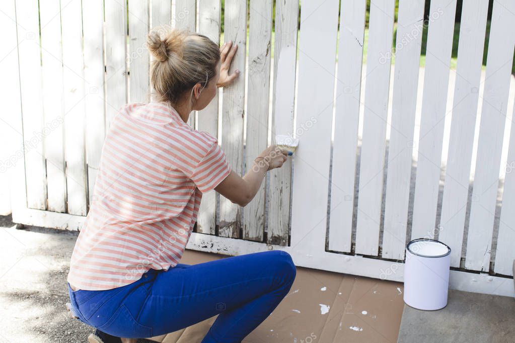 young beautiful woman painting in white color fence at summer 