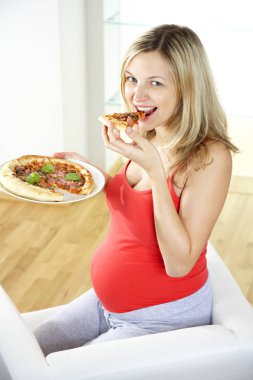 koltukta oturan ve evde pizza yemek mutlu hamile kadın