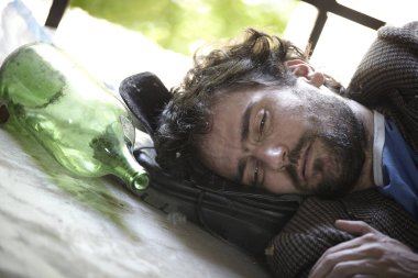 ihmal edilen binada boş alkol şişesi yakınında yerde yatan kirli giysiler içinde sarhoş 