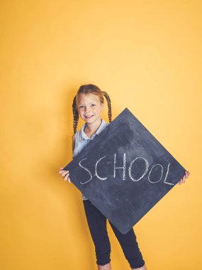 Blackboard kelime okul ile tutarak ve turuncu arka plan önünde poz sarışın kız öğrenci 
