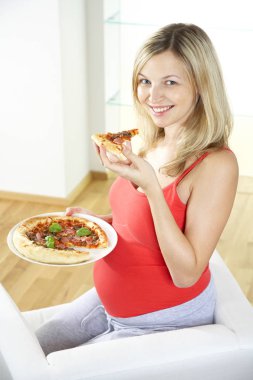 koltukta oturan ve evde pizza yemek mutlu hamile kadın