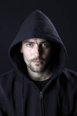 karanlık arka planda kamera bakarak siyah Hood giyen ciddi büyüleyici adam portre 