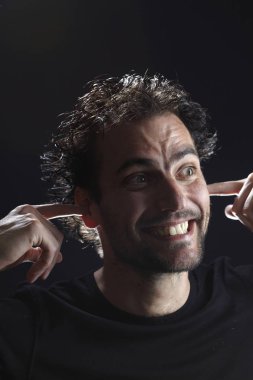 koyu arka planda kulaklarına parmaklar koyarak yakışıklı sakallı adam portre, yakın çekim