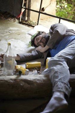 terk edilmiş binada bira bilelerinin yanında yerde uyuyan sarhoş evsiz adam 