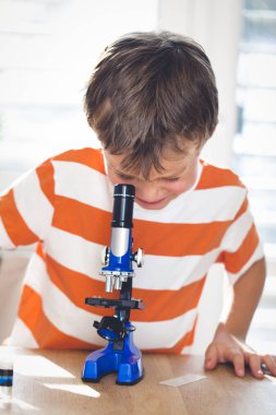 Küçük çocuk evde mikroskop altında slayt bakarak  