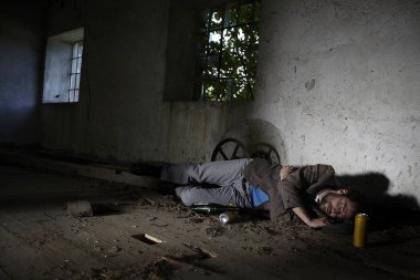 terk edilmiş binada bira bilelerinin yanında yerde uyuyan sarhoş evsiz adam 