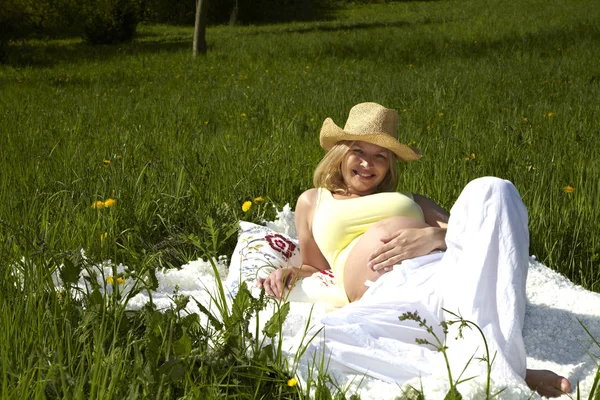 晴れた日に草原に毛布に横たわっている帽子の幸せ妊婦 — ストック写真