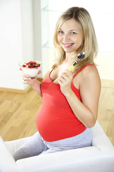 肘掛け椅子に座って 自宅ベリー ヨーグルトで食べて幸せな妊娠中の女性 — ストック写真