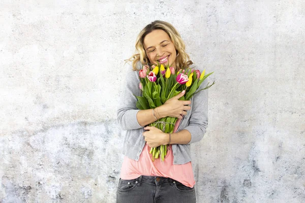 灰色の壁 バレンタインの日の概念の近くに立っている間のチューリップの花の花束を保持している官能的な幸せな女 — ストック写真