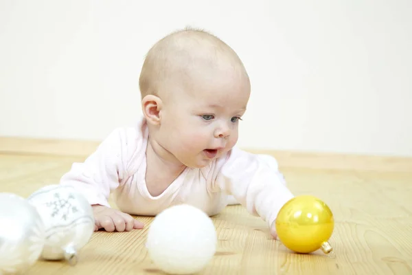 cute little baby in white costume playing with Christmas baubles while lying on floor