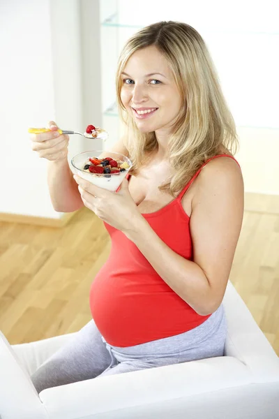 肘掛け椅子に座って 自宅ベリー ヨーグルトで食べて幸せな妊娠中の女性 — ストック写真