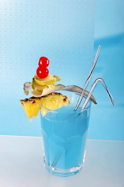 blue cocktail with slice of pineapple and cherries decoration in glass