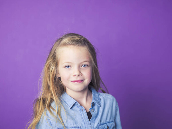 portrait of cute little girl wearing blue denim shirt in front of violet background in studio