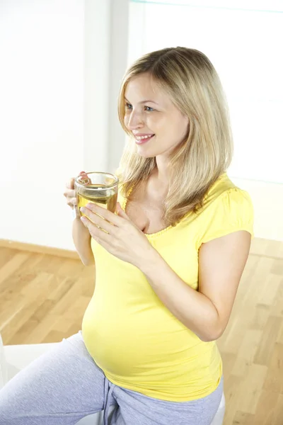 肘掛け椅子に座って ガラスのコップを自宅からお茶を飲んで幸せな妊娠中の女性 — ストック写真