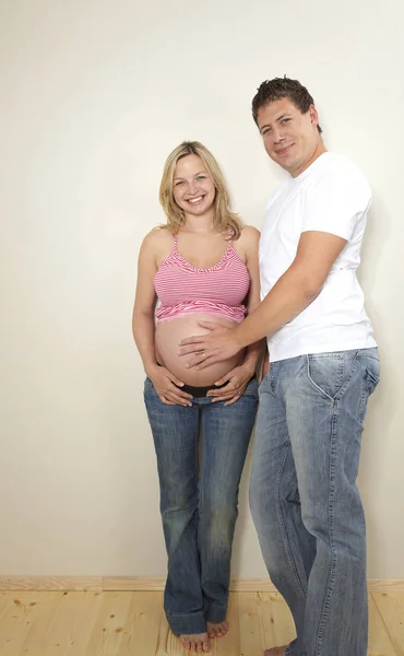 快乐的男人与金发怀孕的妻子摆在一起附近的墙壁在家里 期望概念 — 图库照片