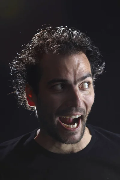 portrait of bearded brunet man with opened mouth grimacing on dark background, close-up