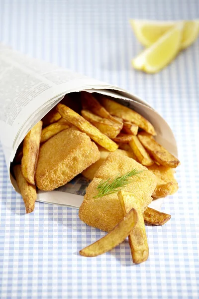 pieces of fish and French fries in newspaper on table, close-up