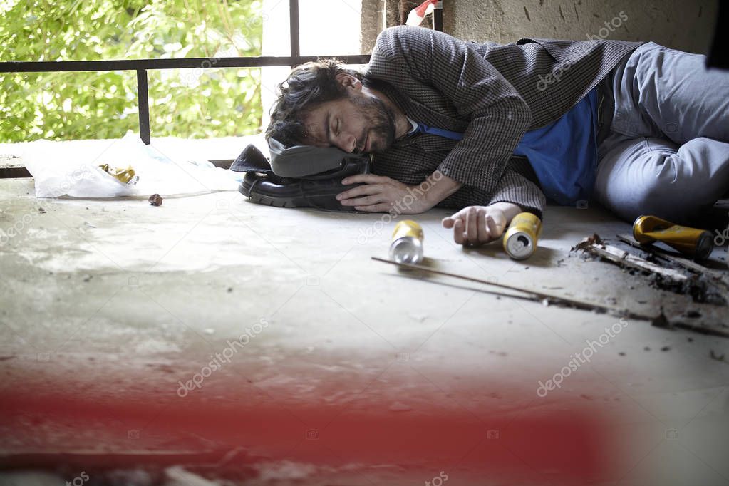 drunk homeless man sleeping on floor near beer cans in abandoned building 