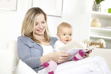 Anne ve meraklı kızı kanepe ve oturma odası, okuma kitabı üzerinde otururken eğleniyor