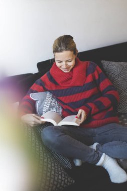 kadın Kırmızı şeritli kazak evde kanepede otururken bir kitap okuma 