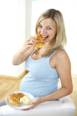 koltukta oturan ve evde plaka kruvasan yemek mutlu hamile kadın