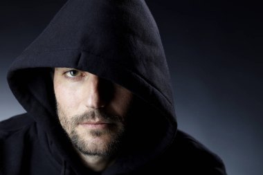 karanlık arka planda kamera bakarak siyah Hood giyen ciddi büyüleyici adam portre 