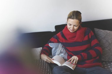 kadın Kırmızı şeritli kazak evde kanepede otururken bir kitap okuma 