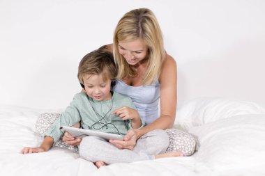 Anne ve oğlu yatak tablet PC'de ve kulaklık ile otururken eğleniyor 