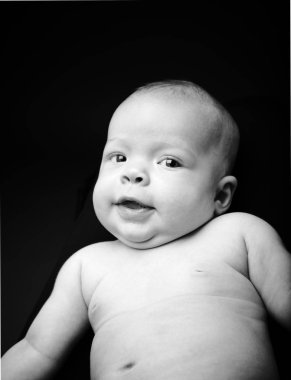 Siyah arka planda poz veren küçük, çıplak, şirin bir bebek.  