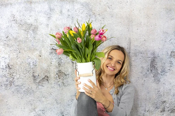 Piękna Kobieta Blonde Holding Dzbanek Kolorowe Tulipany Tle Ścian Betonowych — Zdjęcie stockowe