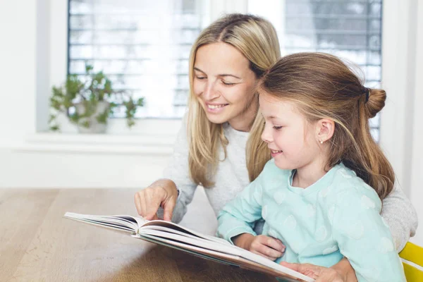 Mother with book teaching daughter to read at home