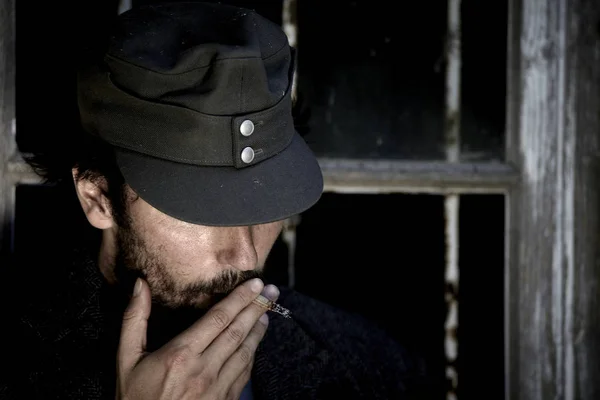 brutal man in cap smoking cigarette on old window background