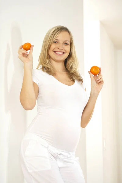 Ξανθιά Έγκυος Γυναίκα Μανταρίνια Χαμογελούν Και Βλέπουν Φωτογραφικών Μηχανών Ενώ — Φωτογραφία Αρχείου