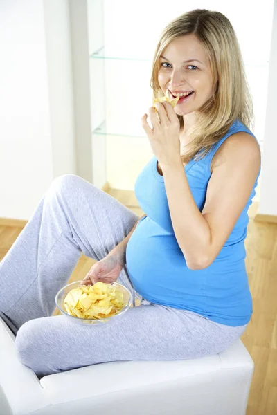 evde mutlu hamile kadın koltukta oturma ve yemek fişleri