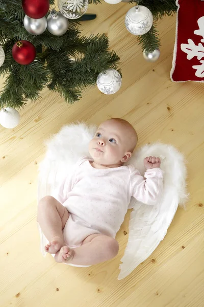 有趣的小婴儿在白色的服装与天使的翅膀躺在地板上 圣诞树附近的小球 — 图库照片
