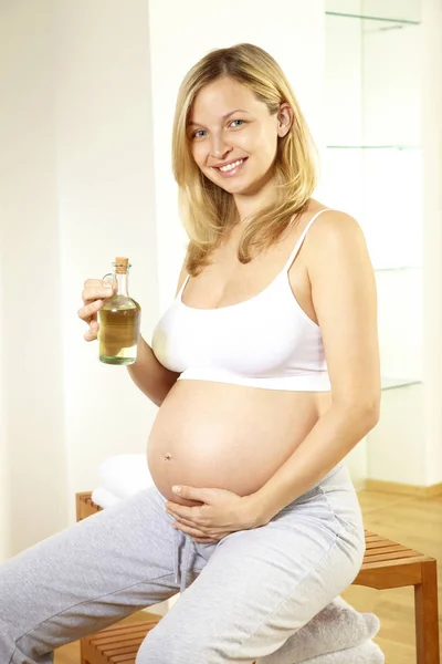 Blond Kobieta Ciąży Sobie Białą Bieliznę Trzymając Butelkę Oliwka Masażu — Zdjęcie stockowe