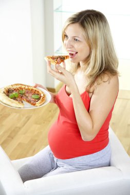 koltukta oturan ve evde pizza yemek mutlu hamile kadın