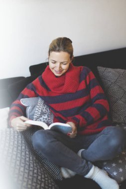kadın Kırmızı şeritli kazak evde kanepede otururken bir kitap okuma 