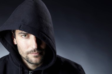 karanlık arka planda kamera bakarak siyah Hood giyen ciddi büyüleyici adam portre 