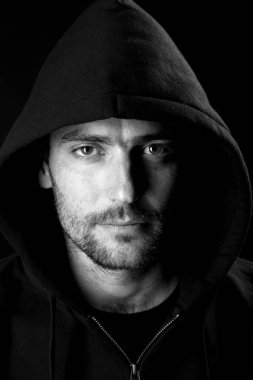 karanlık arka planda kamera bakarak siyah Hood giyen ciddi büyüleyici adam portre 