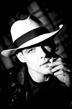 karanlık stüdyo arka planda şapka sigara sigara yakışıklı genç adamın portresi 